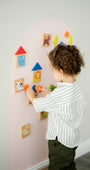 A toddler playing with Tix&Mix magnetic wall decal, arranging colorful geometric shapes and animals set on a pink wall decal.
