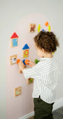 A make toddler playing with wooden magnetic animal puzzle playset on a pink wall decal.