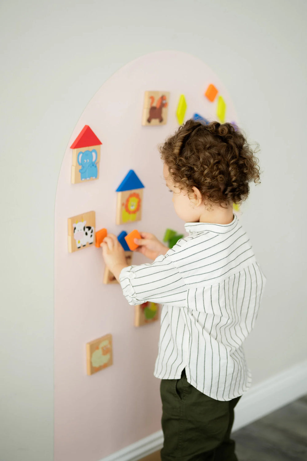 A make toddler playing with wooden magnetic animal puzzle playset on a pink wall decal.