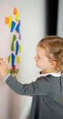 A girl toddler arranging colorful magnetic shapes vertically on a Tix&Mix wall decal.