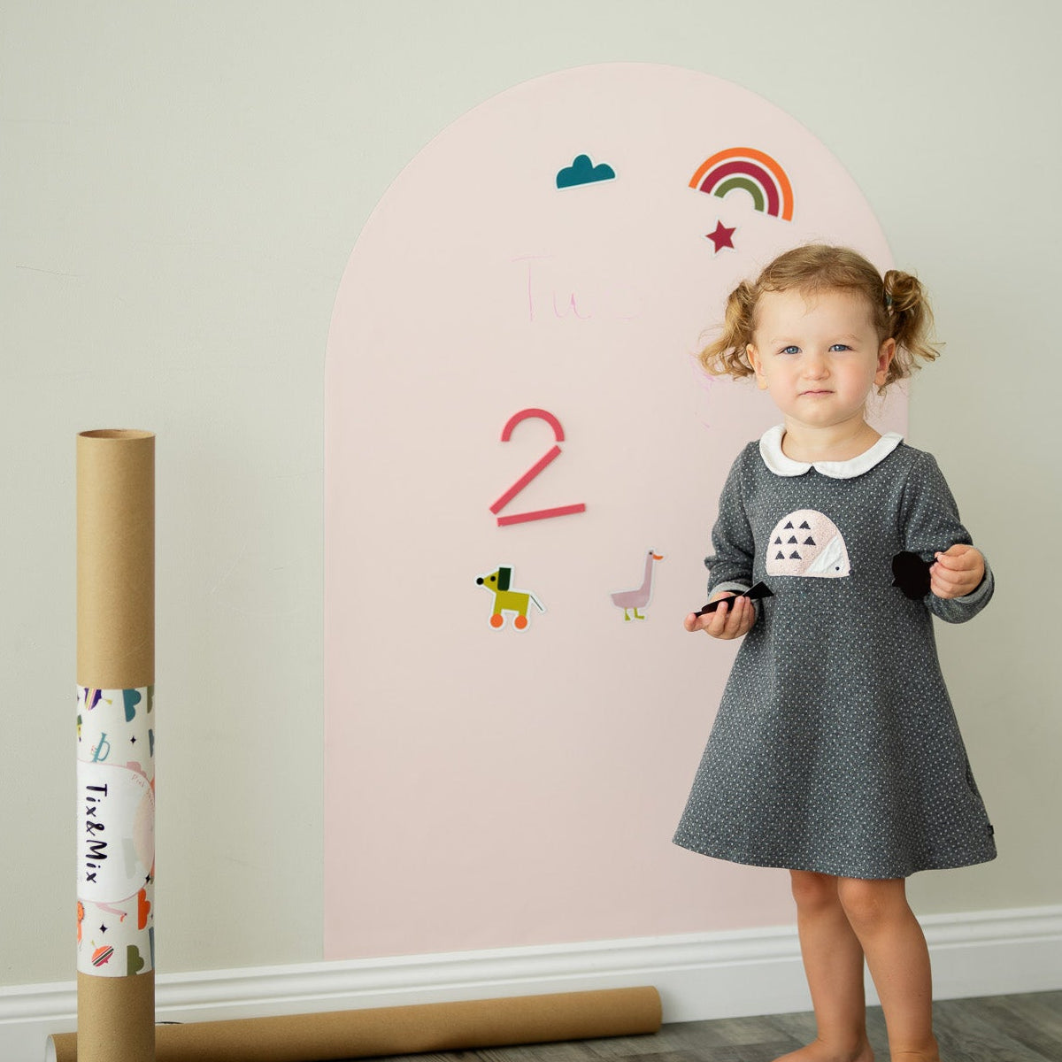 A toddler standing beside a Tix&Mix pink magnetic wall decal in a playroom.