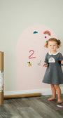 A toddler standing beside a Tix&Mix pink magnetic wall decal in a playroom.