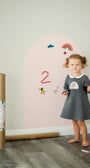 A female kid playing with Tix&Mix magnetic wooden toys on a pink wall decal.