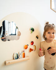 A female toddler looking at the camera while playing with Tix&Mix magnetic foods games set on a white wall decal.
