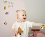 A toddler holding a magnetic giraffe toy while playing with Tix&Mix pink magnetic wall decal.