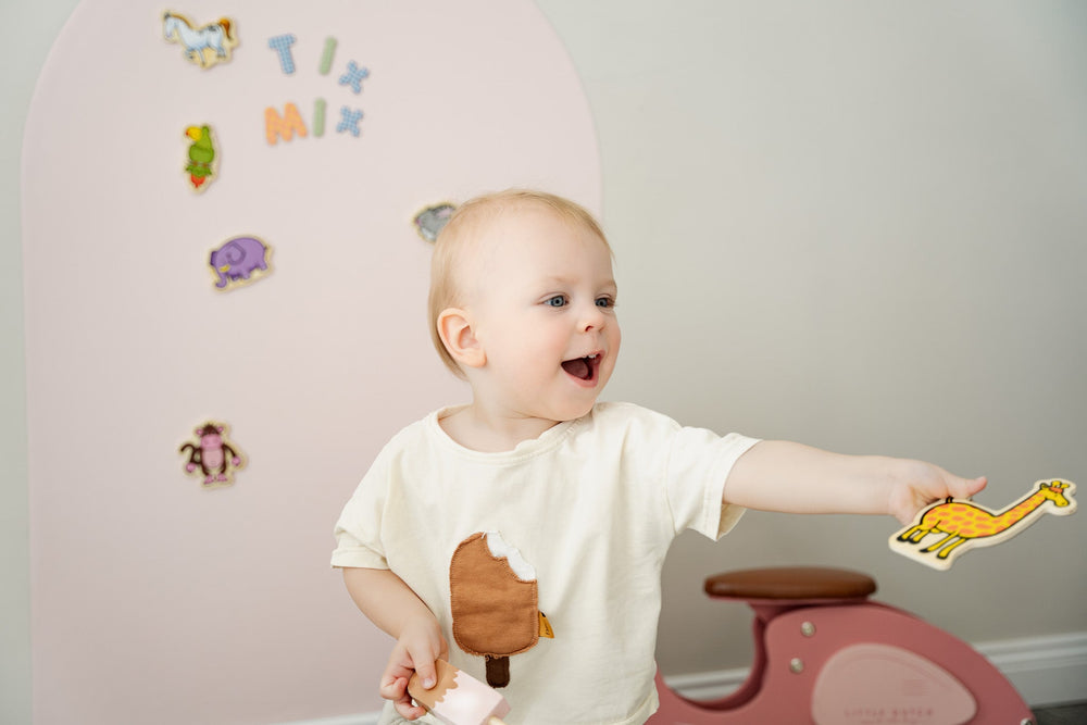 A toddler holding a magnetic giraffe toy while playing with Tix&Mix pink magnetic wall decal.