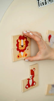 A hand holding a wooden magnetic tiger puzzle set placed on a white wall decal.