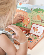 A child playing with Tix & Mix magnetic animal puzzle set, placing farm-themed magnets on a reusable board inside a wooden storage box.