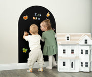 Two toddlers playing with Tix&Mix magnetic toys on a black magnetic wall decal.