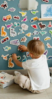 A male kid playing with Tix&Mix magnetic animals and vehicles toys on a cyan wave wall decal.