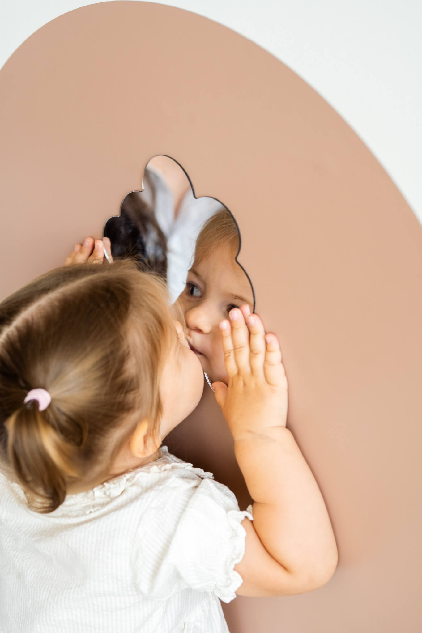 A toddler looking at her reflection on a clean mirror.