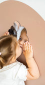 A female toddler looking at her reflection on a Tix&Mix magnetic mirror placed on a brown wall decal.