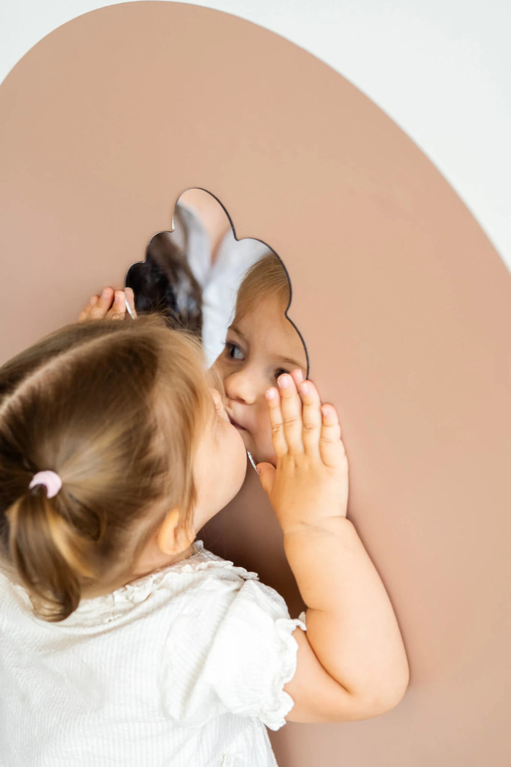 A female toddler looking at her reflection on a Tix&Mix magnetic mirror placed on a brown wall decal.