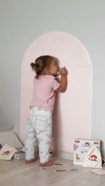 A toddler playing with Tix&Mix magnetic toys on a pink magnetic wall decal.