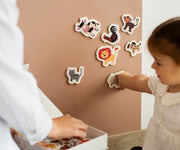 A child playing with Tix&Mix magnetic animal toys on a brown wall decal while being assisted by her parent.
