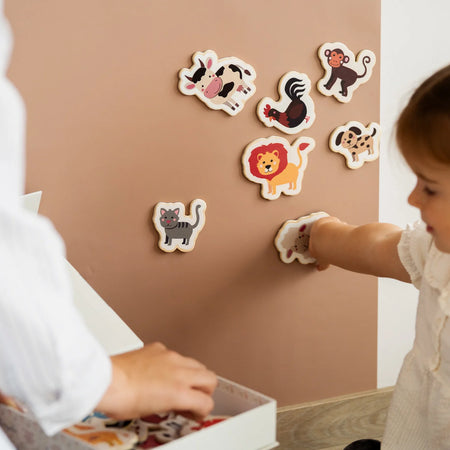 A child playing with Tix&Mix magnetic animal toys on a brown wall decal while being assisted by her parent.