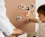 A child playing with Tix&Mix magnetic animal toys on a brown wall decal while being assisted by her parent.